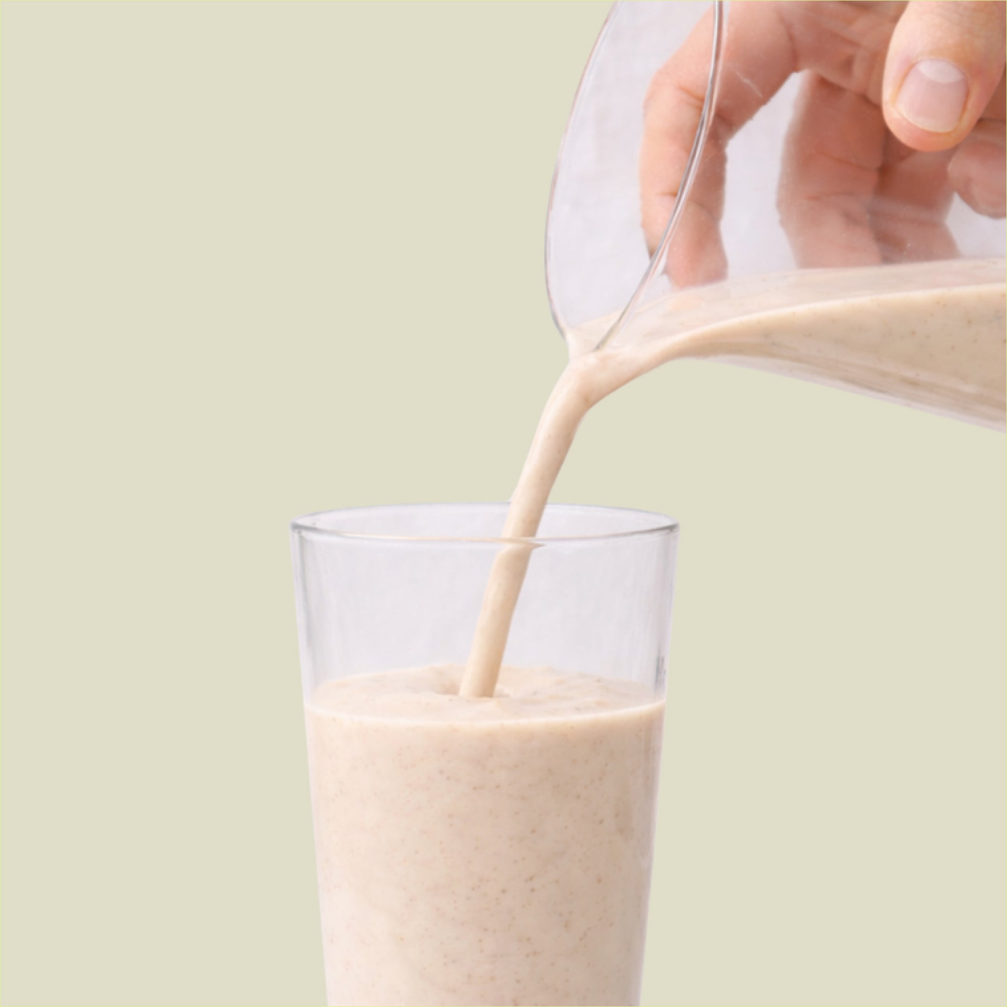 Glass being filled with a creamy liquid against a light green background